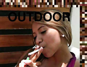Beautiful blonde lady smokes a cigarette outdoors